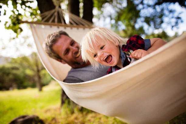 Modern dad hugs his blond child on hammock in garden