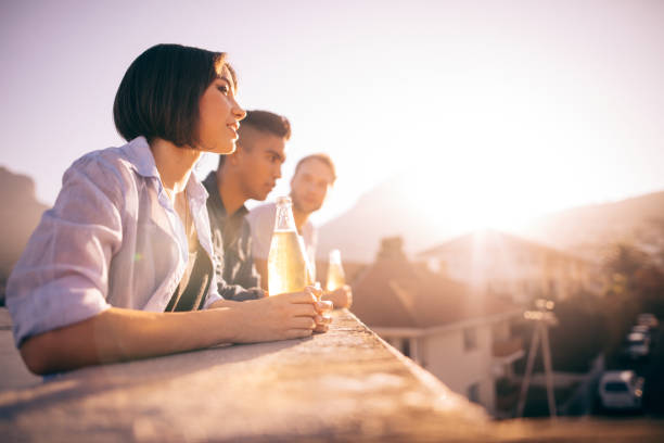 Young Hipster friends drinking beer and talking on the rooftop Group of multi-ethnical hipster friends enjoying the city from the rooftop of a building at sunset with some drinks teenage girls dusk city urban scene stock pictures, royalty-free photos & images