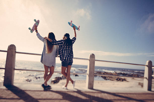 hipster chicas con monopatines en día de verano en la playa - bff fotografías e imágenes de stock