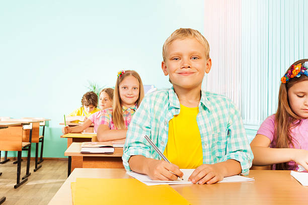 istock Smiling boy sits in class and holds pen to write 517671707