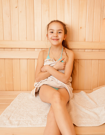 Portrait of smiling little girl sitting on bench at sauna