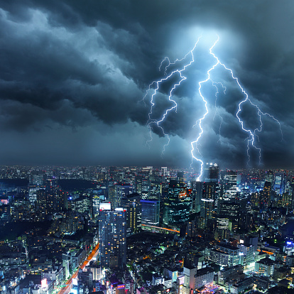 Bright lightnings illuminates a cityscape with skyscrapers, while dark cumulonimbus and clouds hover through the sullen sky. Natural dangers, buildings problems and majestic beauty. Real cloudscape and metropolis panorama with digital lightning. Copy space on image side.