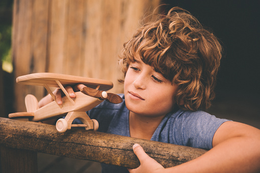 Closeup shot in a vintage style of a young boy in a wooden treehouse daydreaming while playing with his wooden toy plane