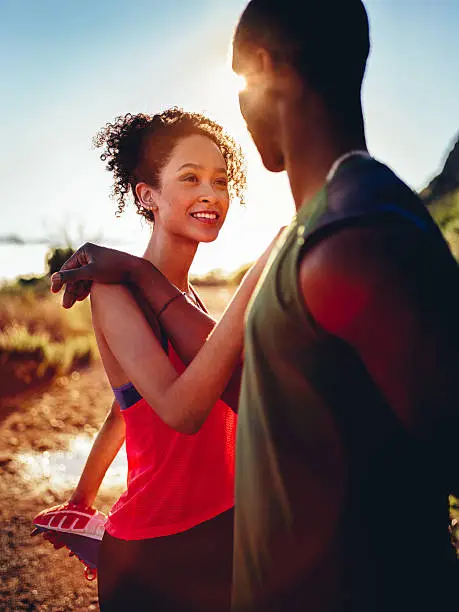 Happy young afro-american couple warming up before jogging outdoors with stretching exercise together