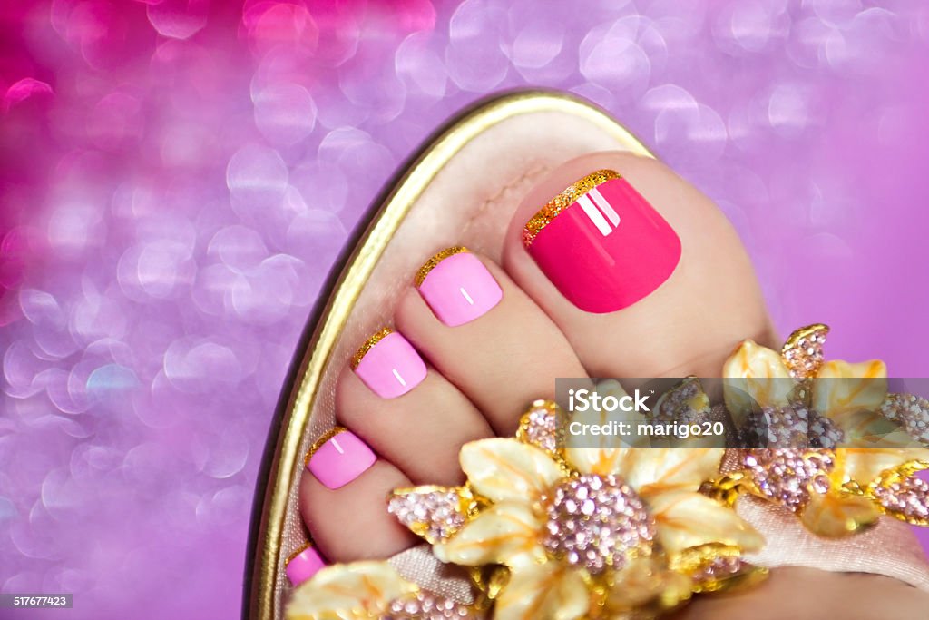 Two-tone pedicure. Two-tone pedicure with Golden stripes on the end of the nail in sandals on a brilliant background. Pedicure Stock Photo