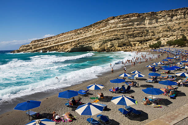 Matala, Greece - August 1, 2014: Many people relaxing at the famous beach of Matala on Crete. Matala is known as former place of pilgrimage for fans of the hippie era. There was a hippie community used to live in the caves above the beach and still there are some hippies around.