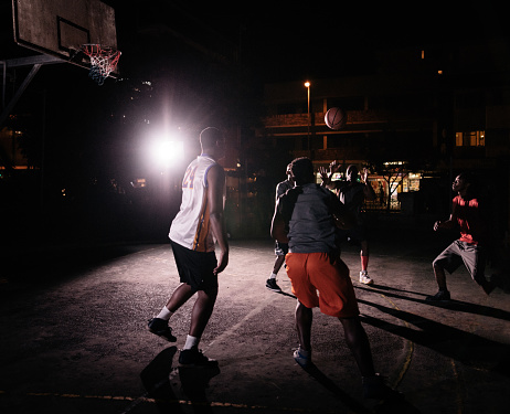 African American basketball players playing in inner-city court during nighttime with single light in background