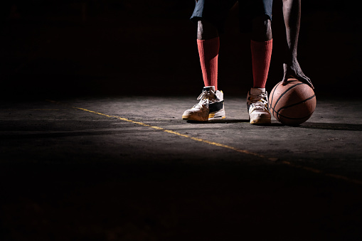 African American basketball player with feet on ground and touching ball on court ground in night with single light source