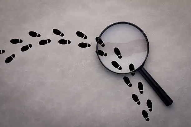 Magnifying glass over footsteps on grey background