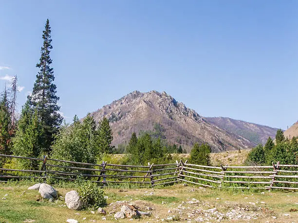 A photo of a ranch, encircled by a split rail fence; located in the mountains of Idaho, and some of the ranch buildings on-site.