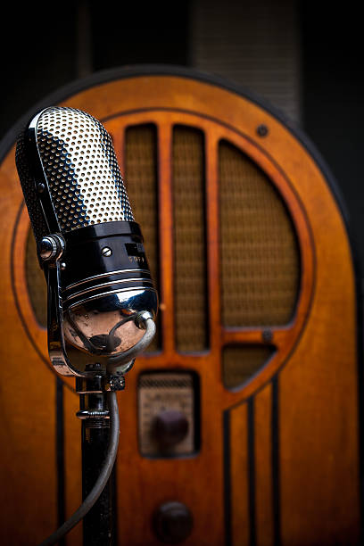 Antique Microphone and Radio A wooden wireless stands behind a shiny microphone, evoking  mid-century radio broadcasting. radio retro revival old old fashioned stock pictures, royalty-free photos & images