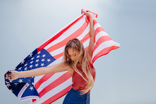 Proud woman with the American flag dancing, isolated on blue wall background
