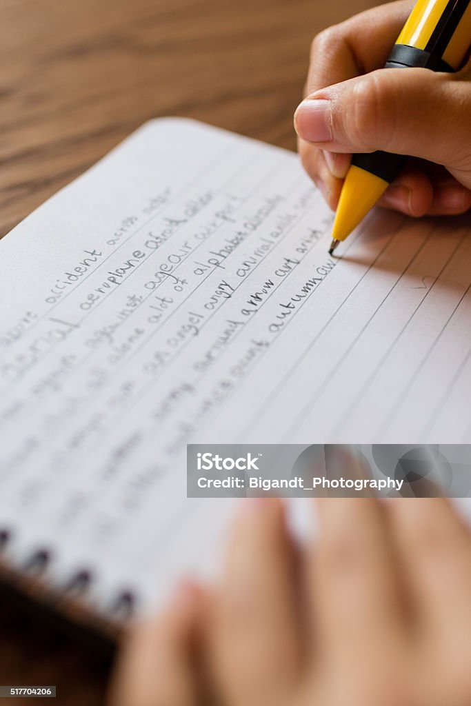 Child writing by hand on notepad Close-up of child hand with refillable pencil writing english words by hand on traditional white notepad paper. Boys Stock Photo