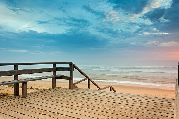 The southern beach of Mimizan Plage. A french travel destination and very popular place for family vacation. Wide beach with fine sand. Sunset with dramatic sky on the evening of a spring day (may). Location: Cote d'Argent, Departement Landes, Aquitaine, France. 110 km south of Bordeaux, 110 km north of Bayonne, Biarritz. In the foreground a wooden stairway down from the dunes to the beach (protection for the sensible vegetation of the dunes).