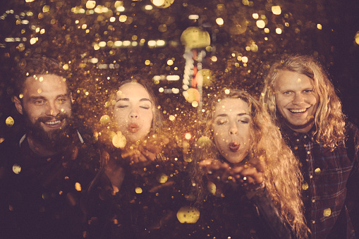 Teenager hipster friends celebrating a night party by blowing golden confetti with city lights in the background