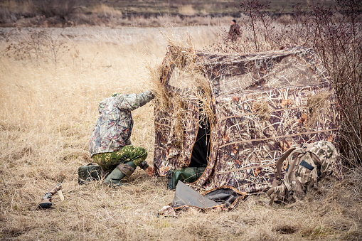 Explorer camouflage his tent in rural field during hunting season