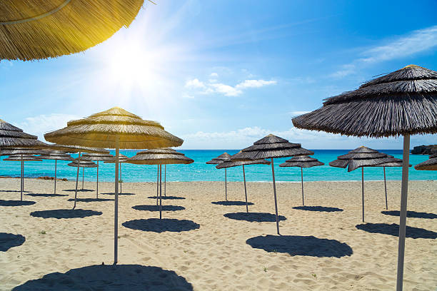 Light blue sky and sea Thatch umbrellas on the beach under a bright sun. The water of the Mediterranean Sea is turquoise, crystal clear and the sand is golden. A few clouds  complete the coastal landscape. cyprus agia napa stock pictures, royalty-free photos & images
