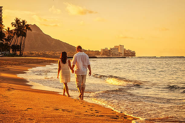Happy Couple Walking on Waikiki Beach at Sunrise Photo of a happy young couple walking hand-in-hand on Waikiki beach at sunrise. big island hawaii islands photos stock pictures, royalty-free photos & images