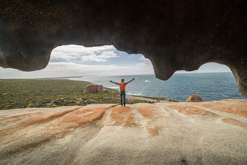 Cheerful young man arms outstretched at The Remarkable rocks, located in Flinder's  chase National park on Kangaroo Island, SA, Australia.