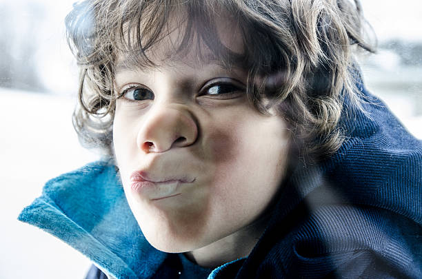 Portrait of a funny boy, he grimaces, shows his tongue and makes horns with his fingers.