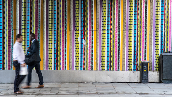 London, England - September 1, 2015: A pair of unidentifiable businessmen pass a colourful stripe mural on Ladbroke Grove in West London.