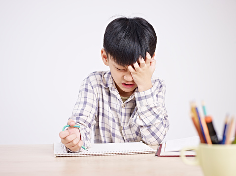 10 year-old asian elementary schoolboy appears to be frustrated while doing homework.
