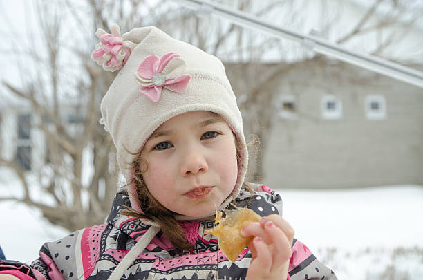 Little girl with hat and red scarf eating Serrano ham.  Children with winter clothes
