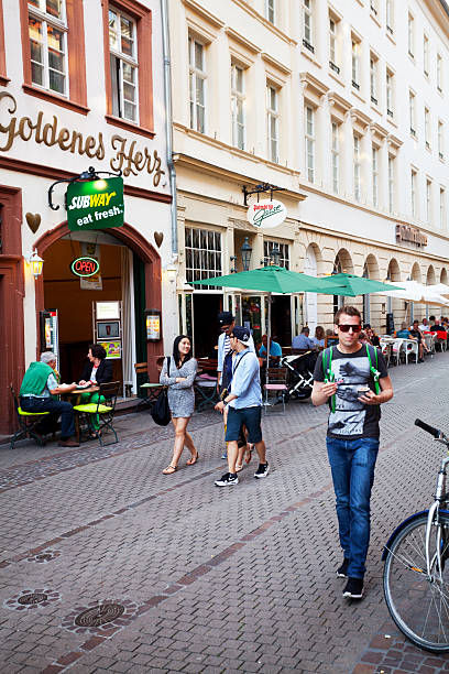 Heidelberg, Germany - June 3, 2015: People and restaurants in street Hauptstraße in Heidelberg in summer. Some asian tourists are walking in street. At left side is restaurant Goldenes Herz.