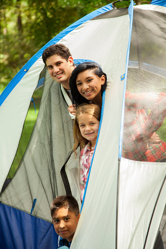 Latin family of four camping outdoors in a national park. Forest area with tent.  They peek out of their tent door.