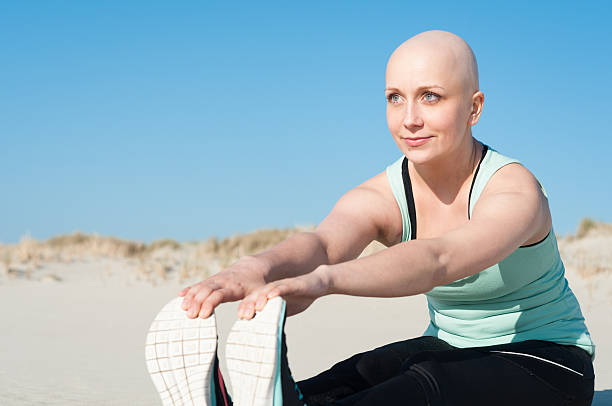 young woman with bald head doing sports Young beautiful woman is stretching on the beach after enduring chemotherapy because of cancer. Sport is most important to get through the rough therapy and to face a positive and healthy future. lymphoma photos stock pictures, royalty-free photos & images