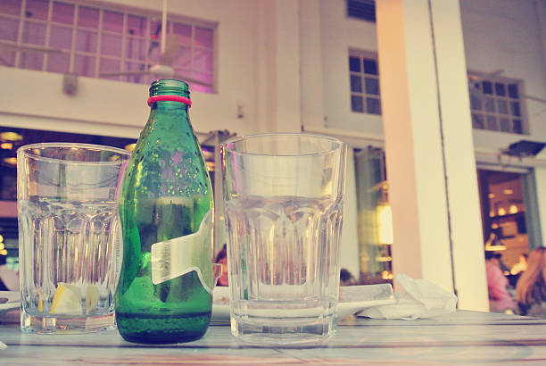 Empty mineral water bottle and two glasses on the table in an open air cafe or restaurant, in the evening. Image filtered in faded, retro style with soft focus; modern urban lifestyle concept.