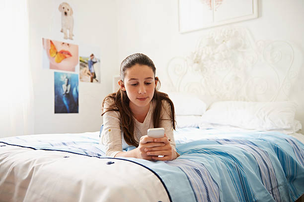 Connection is everything Shot of a teenage girl lying on her bed and texting on her phone 13 14 years child teenage girls lying down stock pictures, royalty-free photos & images