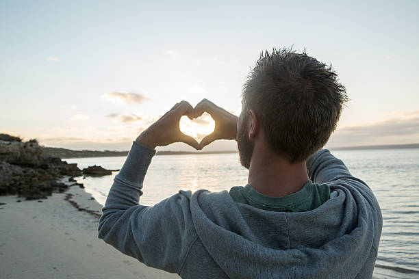 istock Young man on beach makes heart shape finger frame 517750322