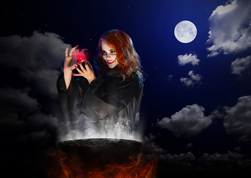 Young witch with red potion and cauldron on night sky background