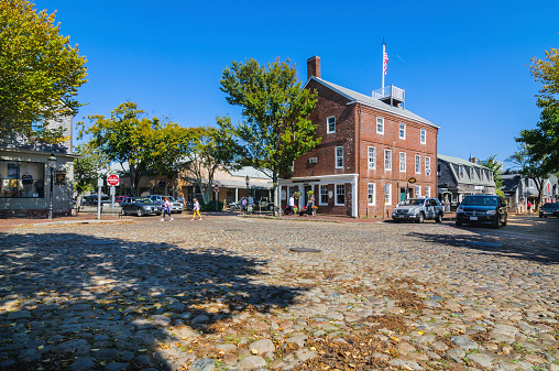 Nantucket, Massachusetts, USA - September 28, 2014: Shoppers stroll the brick sidewalks and cobble stone streets of Nantucket Village on a late September  afternoon as vehicular traffic moves slowly through the intersection. There are no traffic lights anywhere on this quiet island off the Massachusetts Coast.
