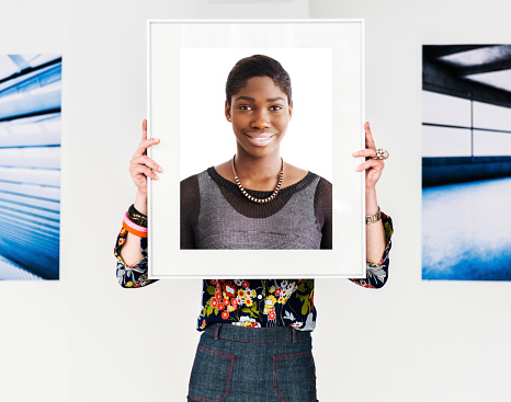 Female artist holding picture frame with portrait of young african woman off her face.