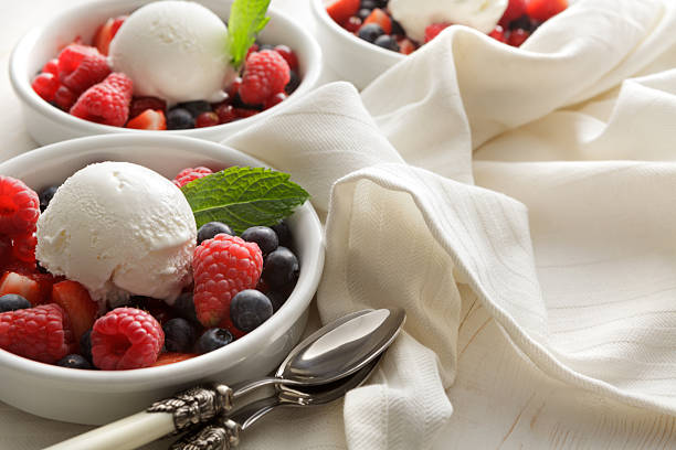 A tempting dessert is served in a clear cup, featuring creamy ice cream topped with fresh raspberries, slices of fig, and vibrant lime, perfect for a joyful gathering.