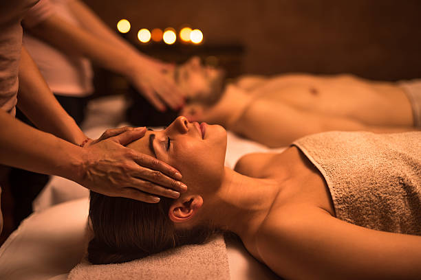Young woman at the spa enjoying in head massage. Couple relaxing at the spa during facial massage. Focus is on foreground, on young woman enjoying with eyes closed. spa stock pictures, royalty-free photos & images