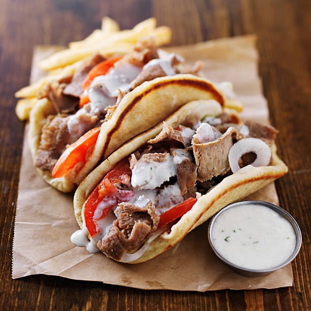 greek gyros with tzatziki sauce greek gyros with tzatziki sauce and fries on parchment paper. Shot with selective focus in natural light. greek food stock pictures, royalty-free photos & images