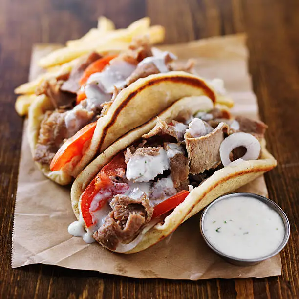 greek gyros with tzatziki sauce and fries on parchment paper. Shot with selective focus in natural light.