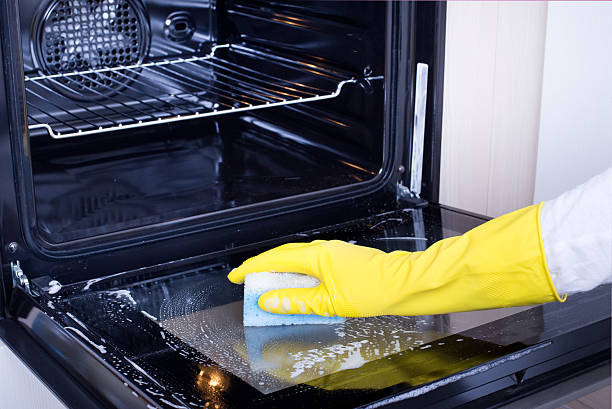 Woman cleaning oven Close up of female hand with yellow protective gloves cleaning oven door oven door stock pictures, royalty-free photos & images