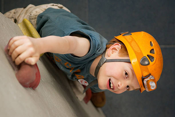 An 8 year old boy wearing a safety helmet climbing on an indoor rock climbing wall, viewed from above.