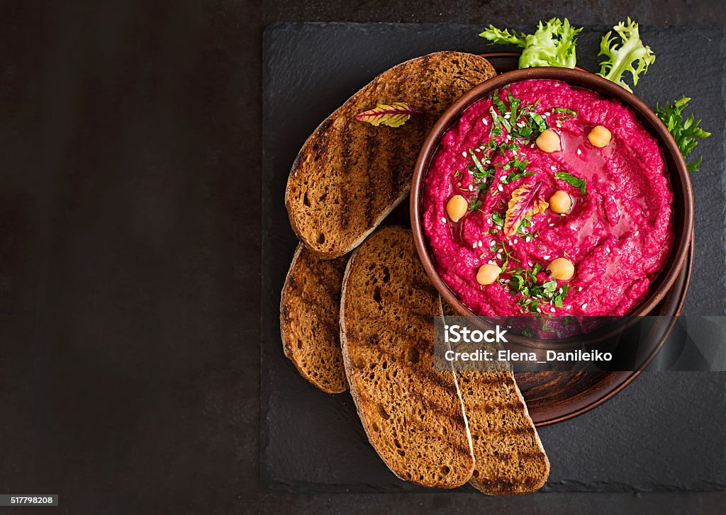 Roasted Beet Hummus with toast in a ceramic bowl Roasted Beet Hummus with toast in a ceramic bowl on a dark background. Top view Hummus - Food Stock Photo