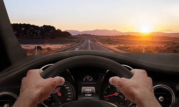 Driving at sunset. View from the driver angle while hands on the wheel.