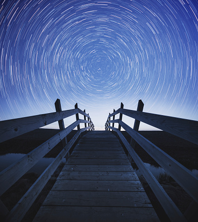 Earth's axis is revealed in the stars above a wooden boardwalk leading to a beach.  Composite image.