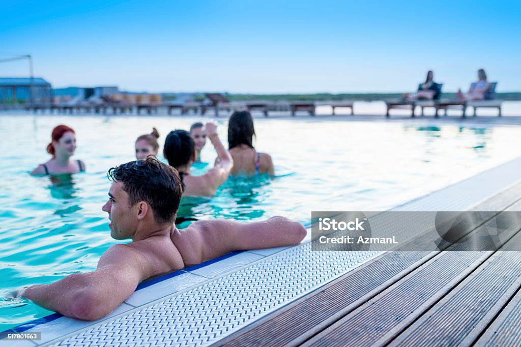 Relaxing in a pool on summer vacation Young people enjoying in a swimming pool and on deck chairs by the pool. Pool Party Stock Photo