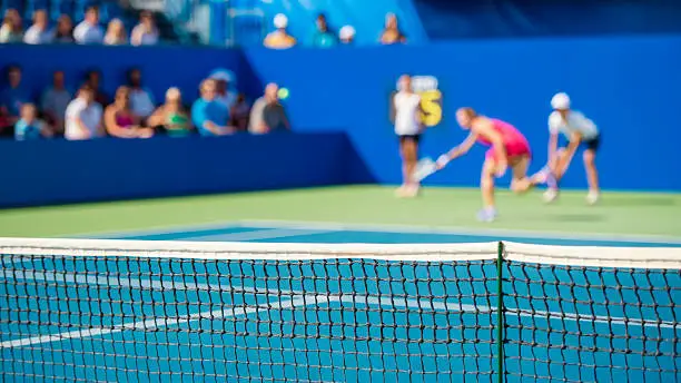 Female tennis player, spectators in the background, focus on net.