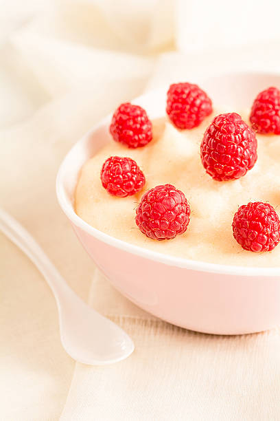 Semolina porridge with fresh raspberries in a bowl stands on a white wooden board.