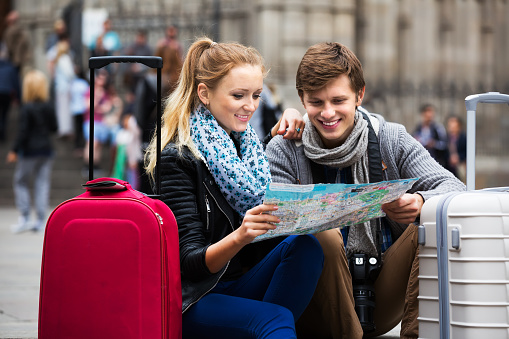 Portrait of smiling couple with luggage checking direction in map outdoors. Focus on woman