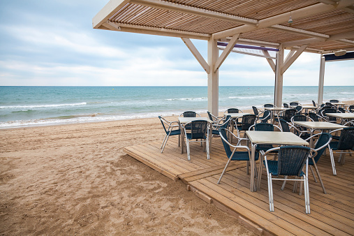 Sea side bar interior with wooden floor and metal armchairs on the sandy beach in Spain